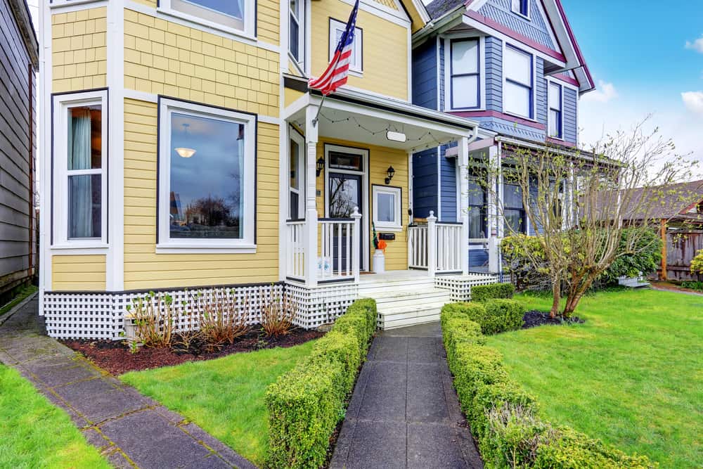 Exterior of yellow family house with American flag. Concrete walkway lead to small covered porch. Northwest, USA